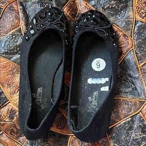 Black flat ballerinas with black shiny embellishments.
6